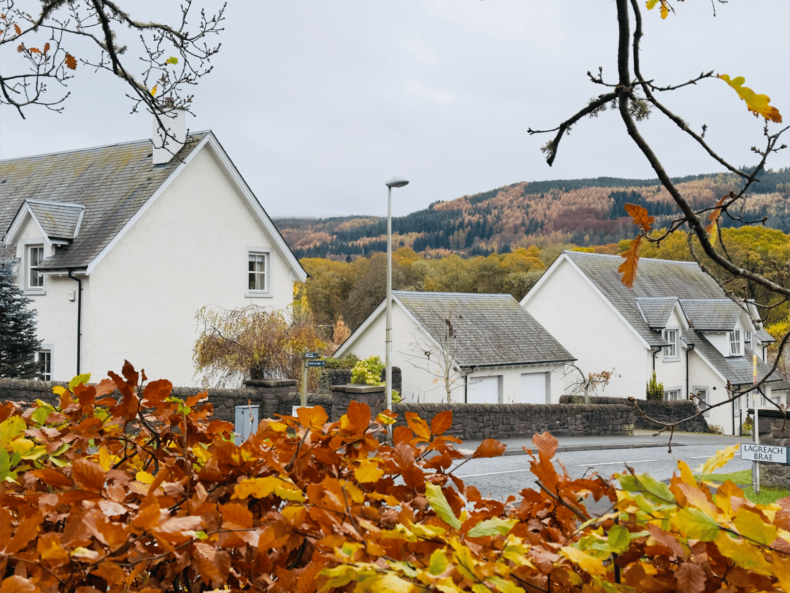 Pitlochry, Scotland during November autumn, with mist covering colorful forested hills and stone cottages in the foreground.